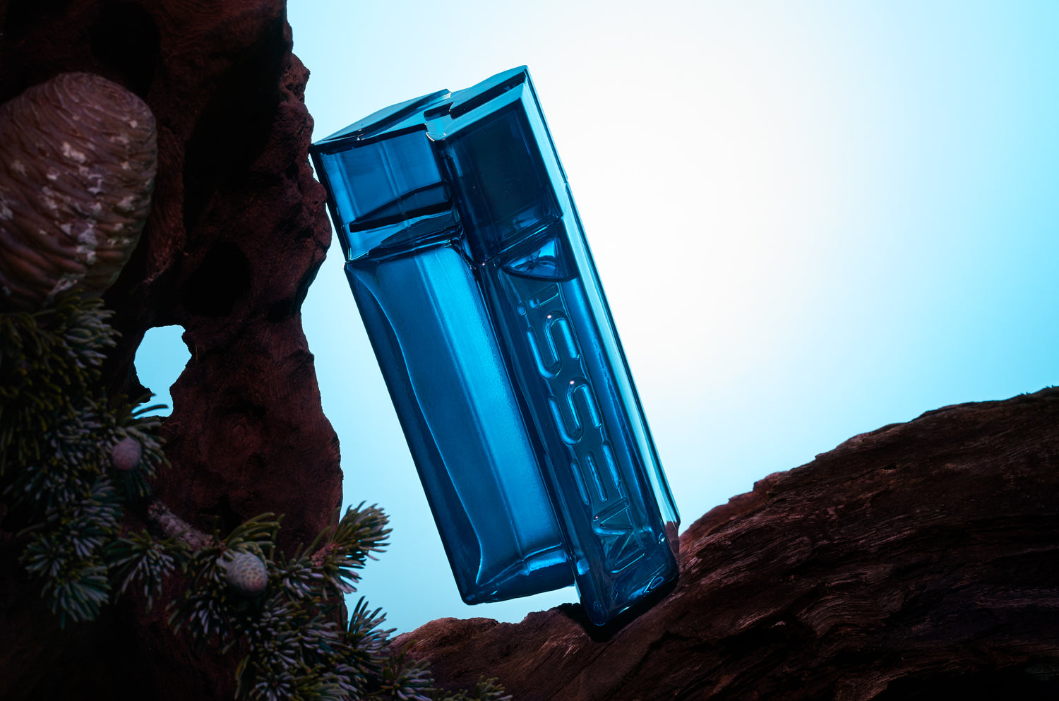 Messi Eau de Parfum bottle tilted on a tree branch with plants surrounding it, illuminated by soft blue light.