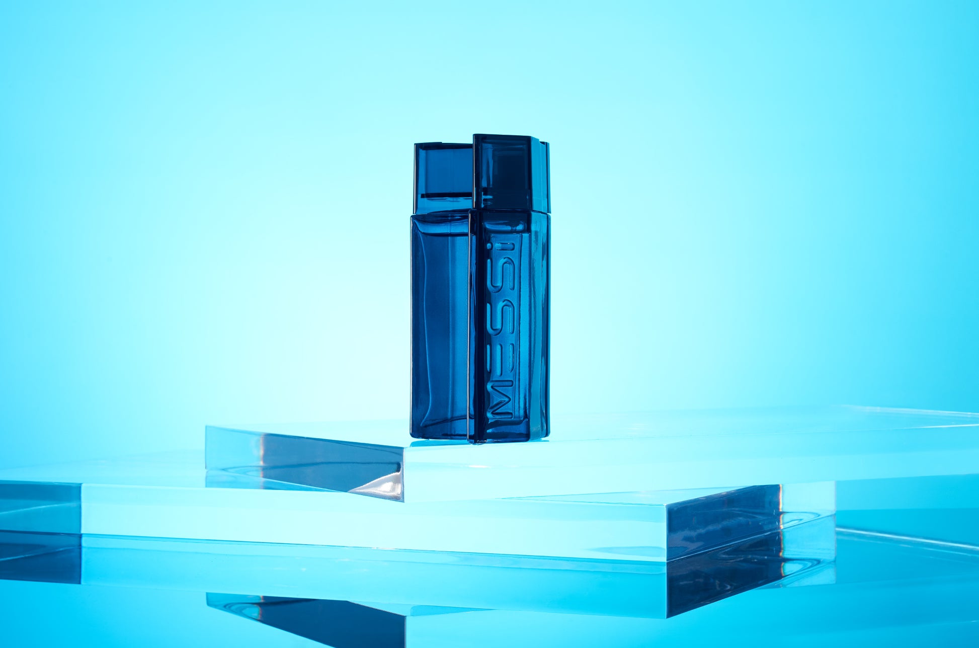 Messi Eau de Parfum bottle displayed on clear glass platforms with a bright blue background.